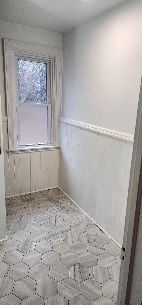 Small, white bathroom with hexagon tile floor, window, and wainscoting.