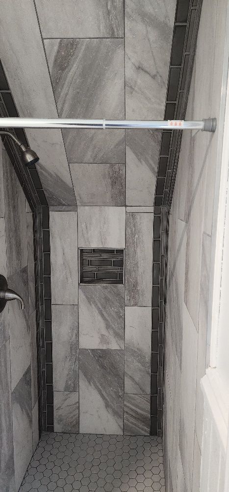 A tiled shower interior with gray and dark trim, shower head, and soap niche.