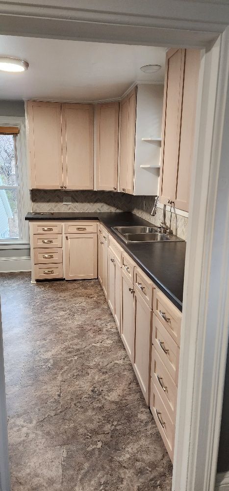Kitchen with beige cabinets, black countertop, stainless steel sink, and gray flooring.