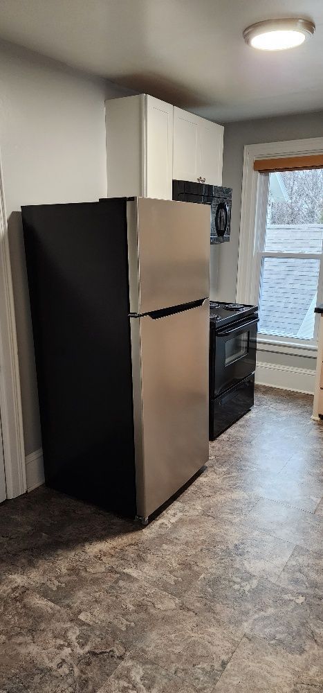 Kitchen with black and stainless steel refrigerator, black stove, cabinets, and a window.