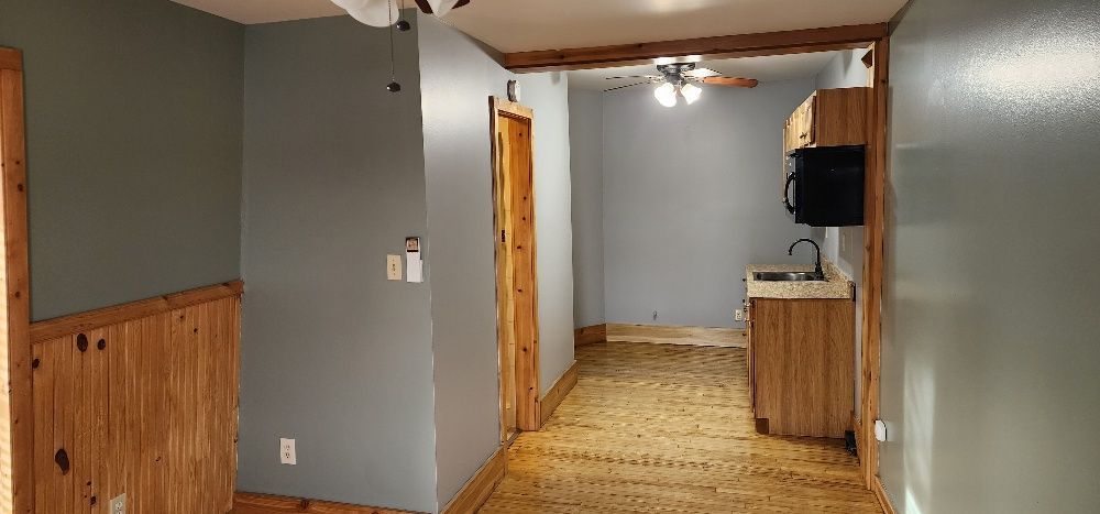 Interior view of a room with wood paneling and gray walls. A kitchen area with cabinets and appliances is visible.