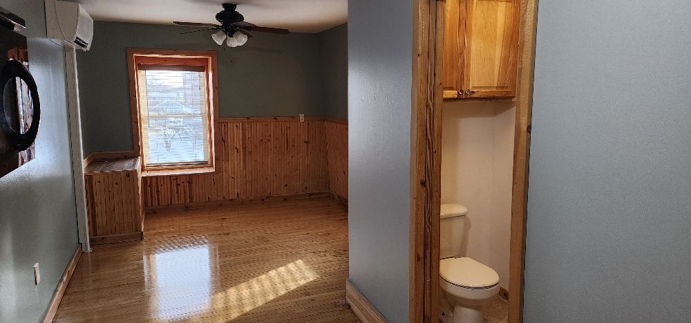 Room interior with a toilet, wood paneling, and a window.