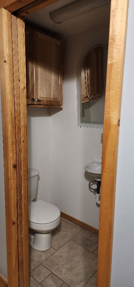 View from a doorway into a small bathroom with a toilet, sink, and cabinets.