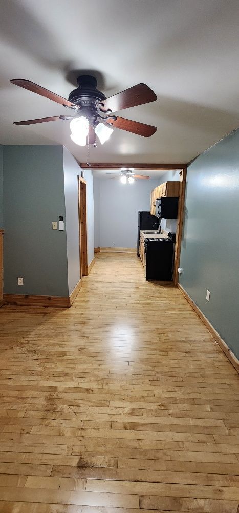 Interior view of a long hallway with hardwood floors and light blue walls, kitchen at the end.