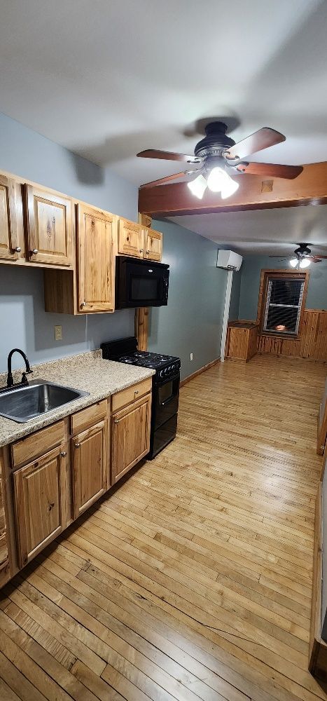 Kitchen with wooden cabinets, black appliances, and light wood floors. Ceiling fans present.