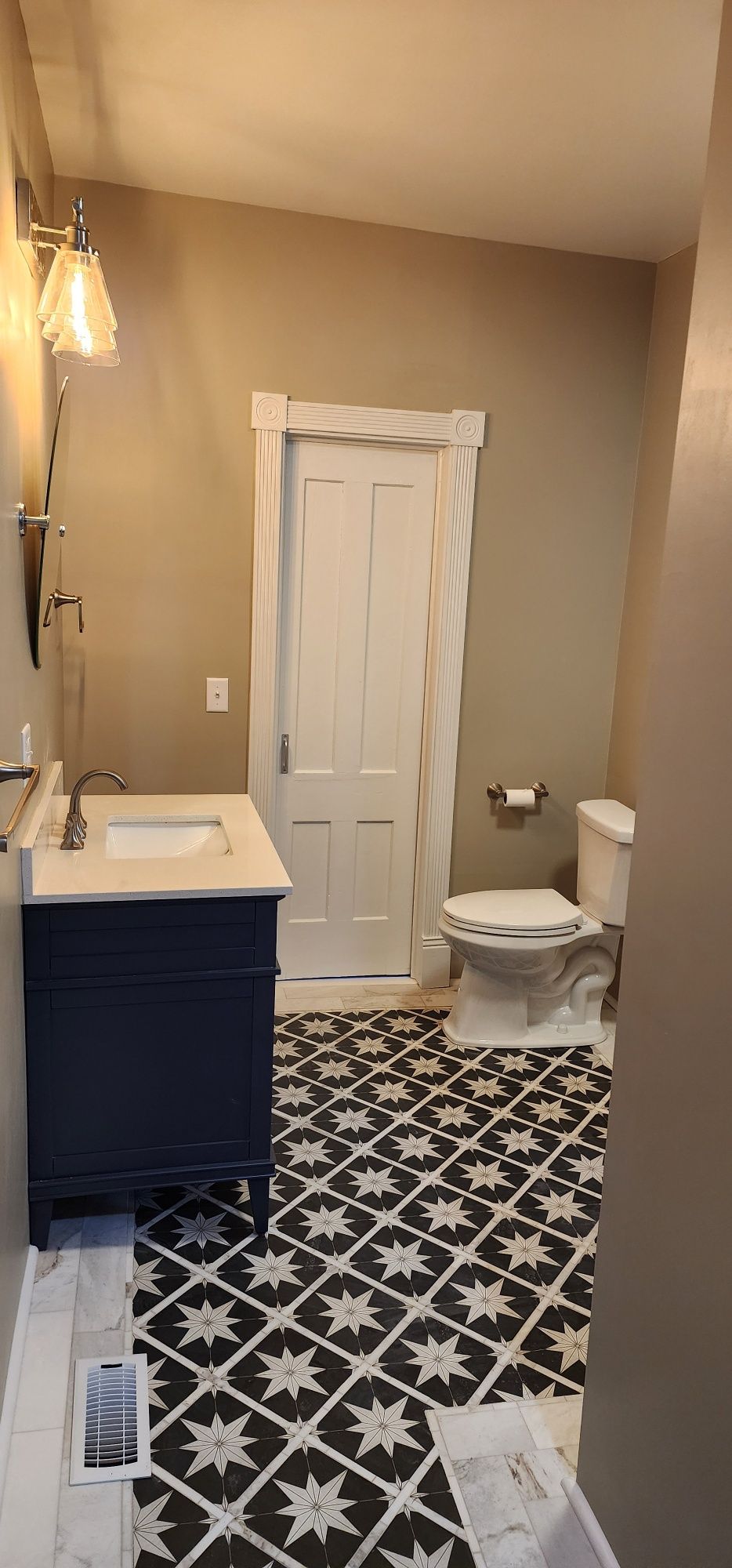 Bathroom with navy vanity, star patterned tile, toilet, and white door.