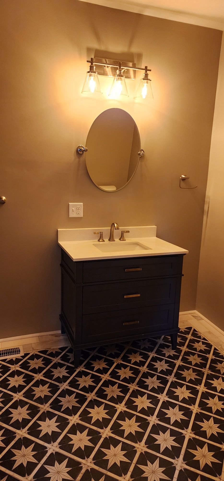Bathroom with dark vanity, oval mirror, and patterned tile floor.