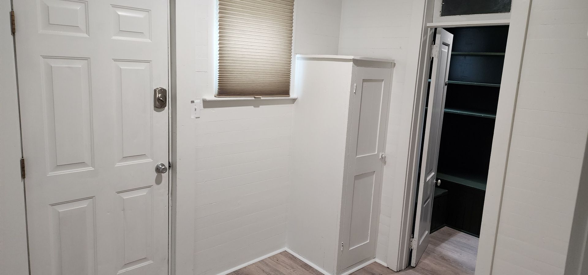 Interior view of a small hallway with a closed white door, a narrow white cabinet, and an open closet.