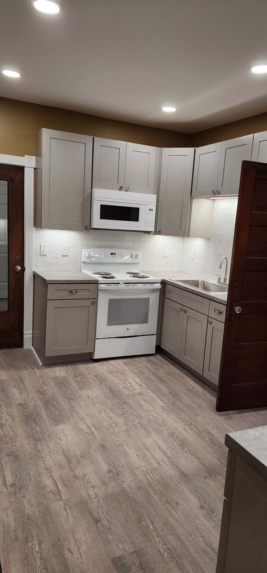 A small kitchen with gray cabinets, white appliances, and wood-look flooring.