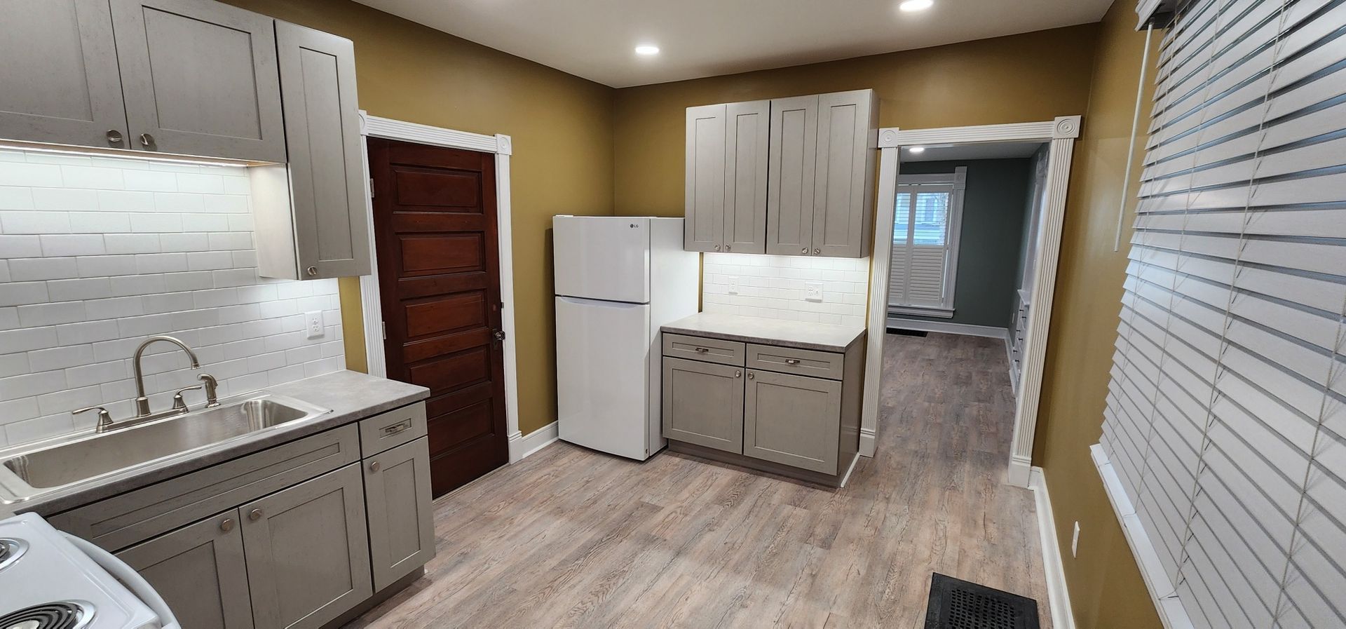 Kitchen interior with cabinets, refrigerator, and doorway to another room. Light grey cabinets and white appliances.