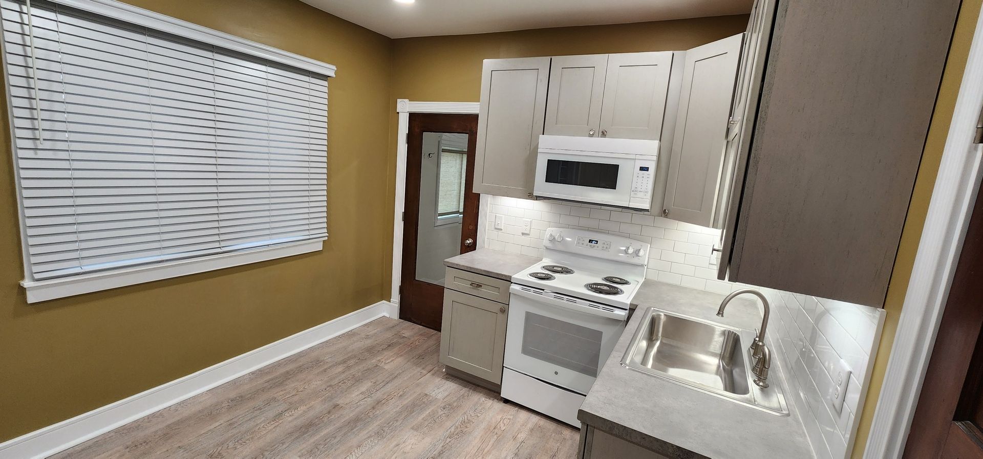 Kitchen with white cabinets, stove, microwave, and sink. Yellow walls, blinds.
