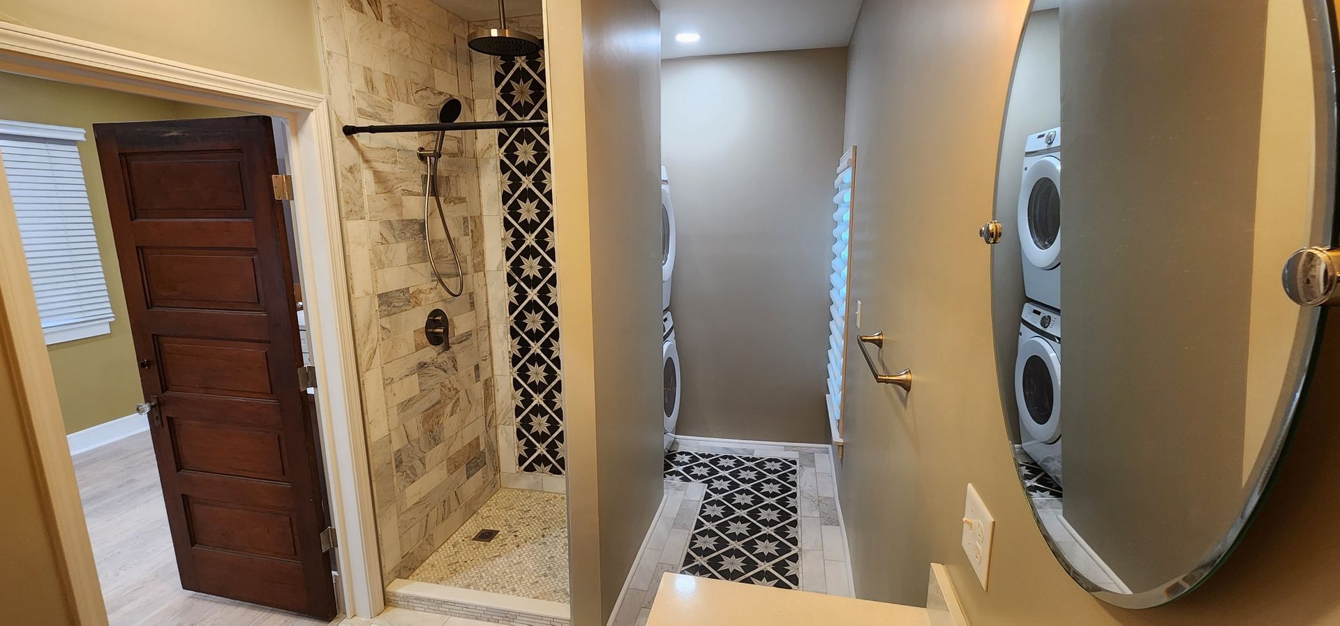 Bathroom with shower, mirror, and a wood door, mostly neutral colors.