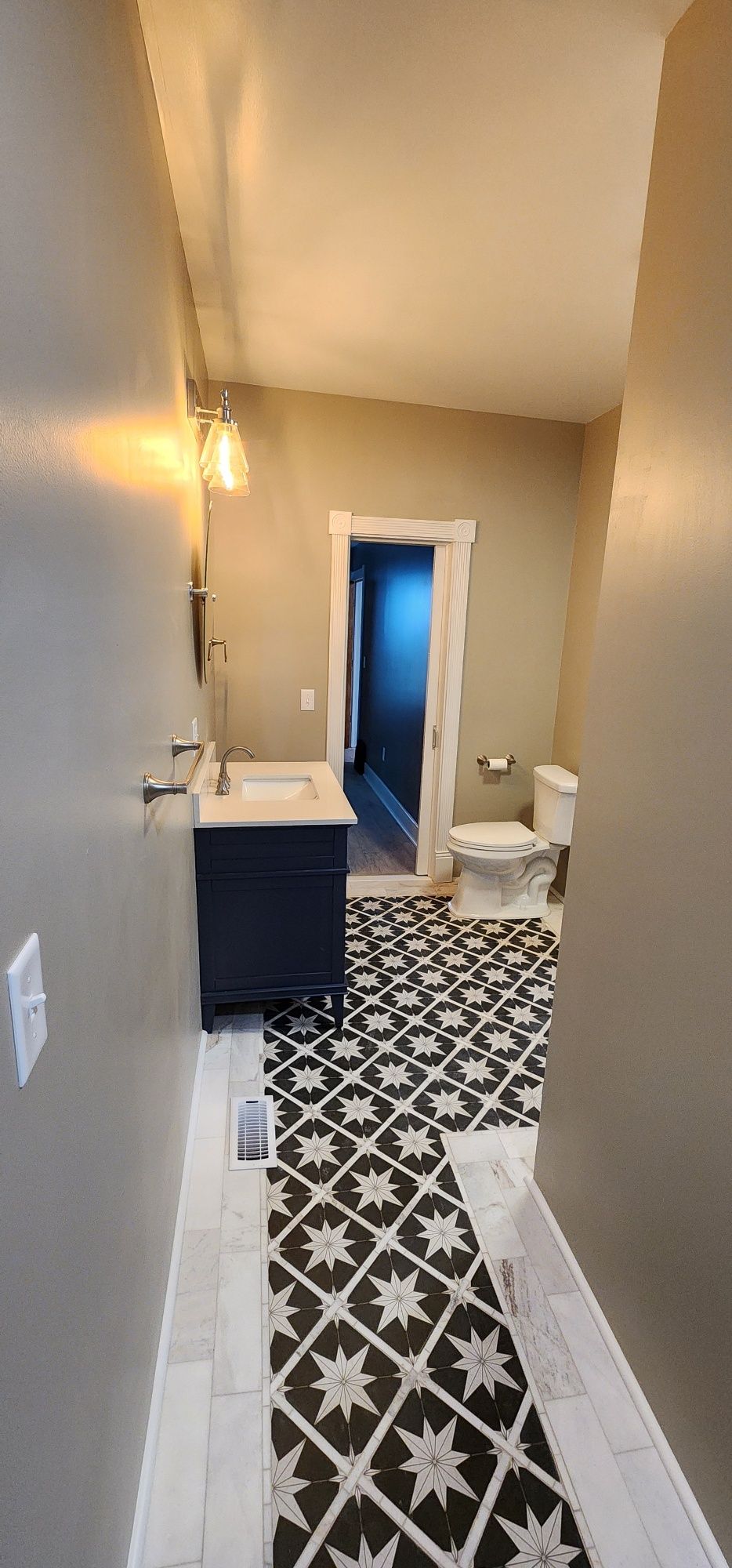 Bathroom with black and white patterned tile floor, dark vanity, and toilet.
