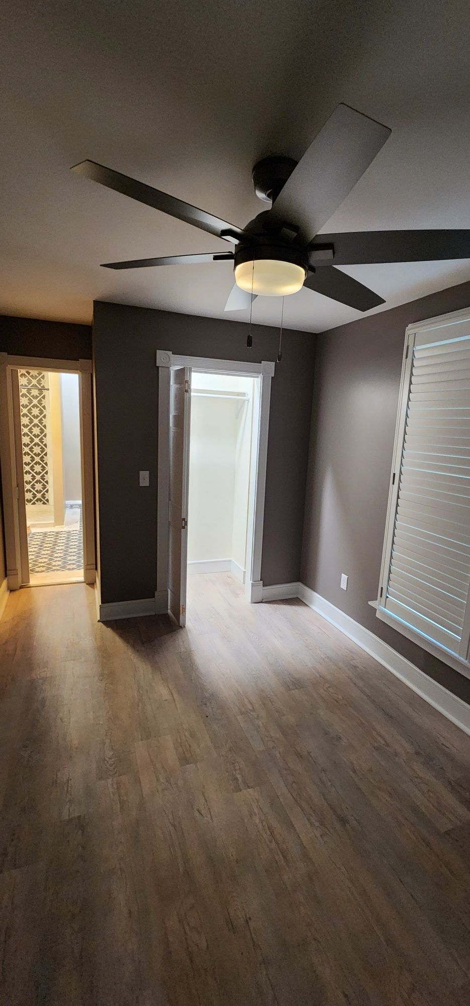 Bedroom with open doors to bathroom and closet, dark ceiling fan, and wood-look flooring.