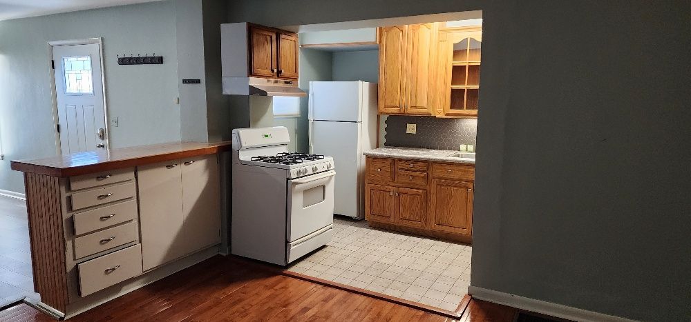 Kitchen with light wood cabinets, white appliances, and a hardwood floor. A rug is in front of the oven.