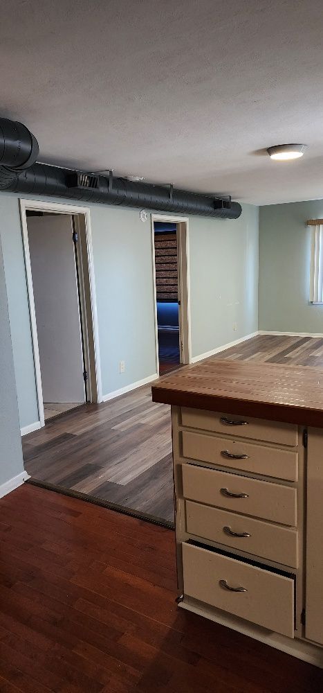 Kitchen interior with wooden floors and cabinets. Two doorways lead to other rooms.  A metal vent pipe runs across the ceiling.