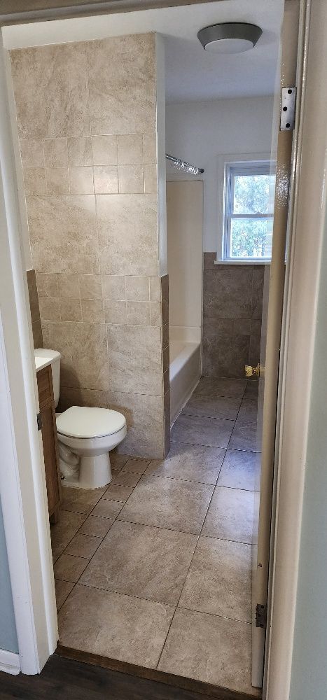 Bathroom interior with a toilet, tiled floor, and shower. The doorway is on the right.