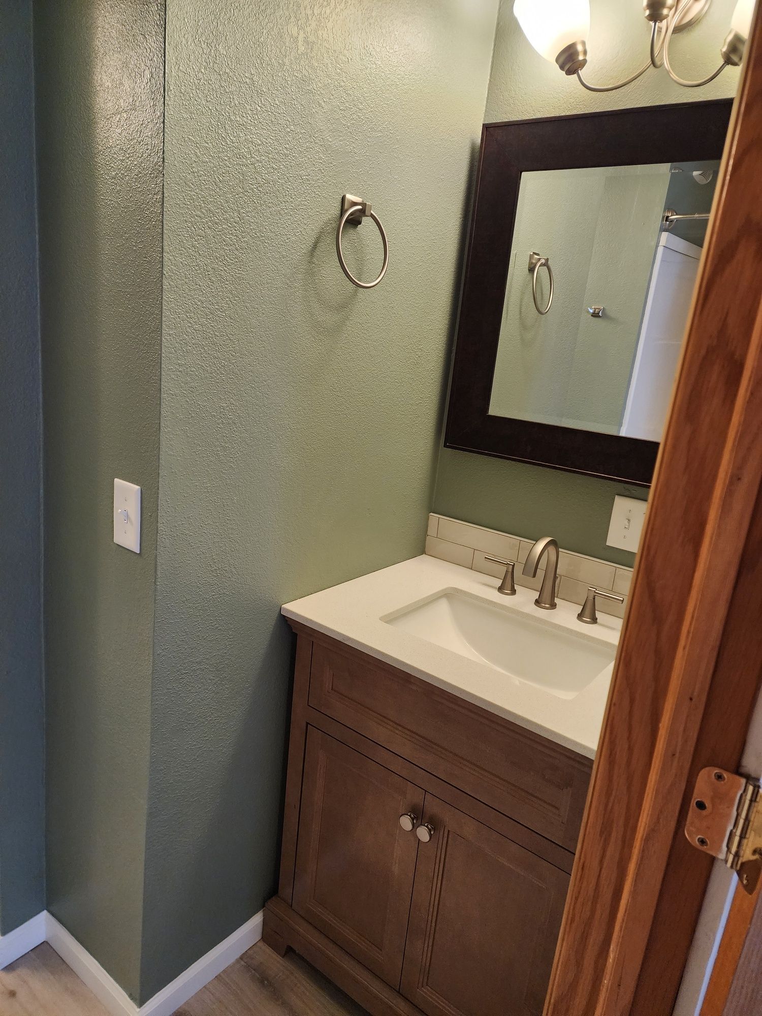 Bathroom with vanity, mirror, and towel ring. Light green walls, wooden cabinet and door frame.