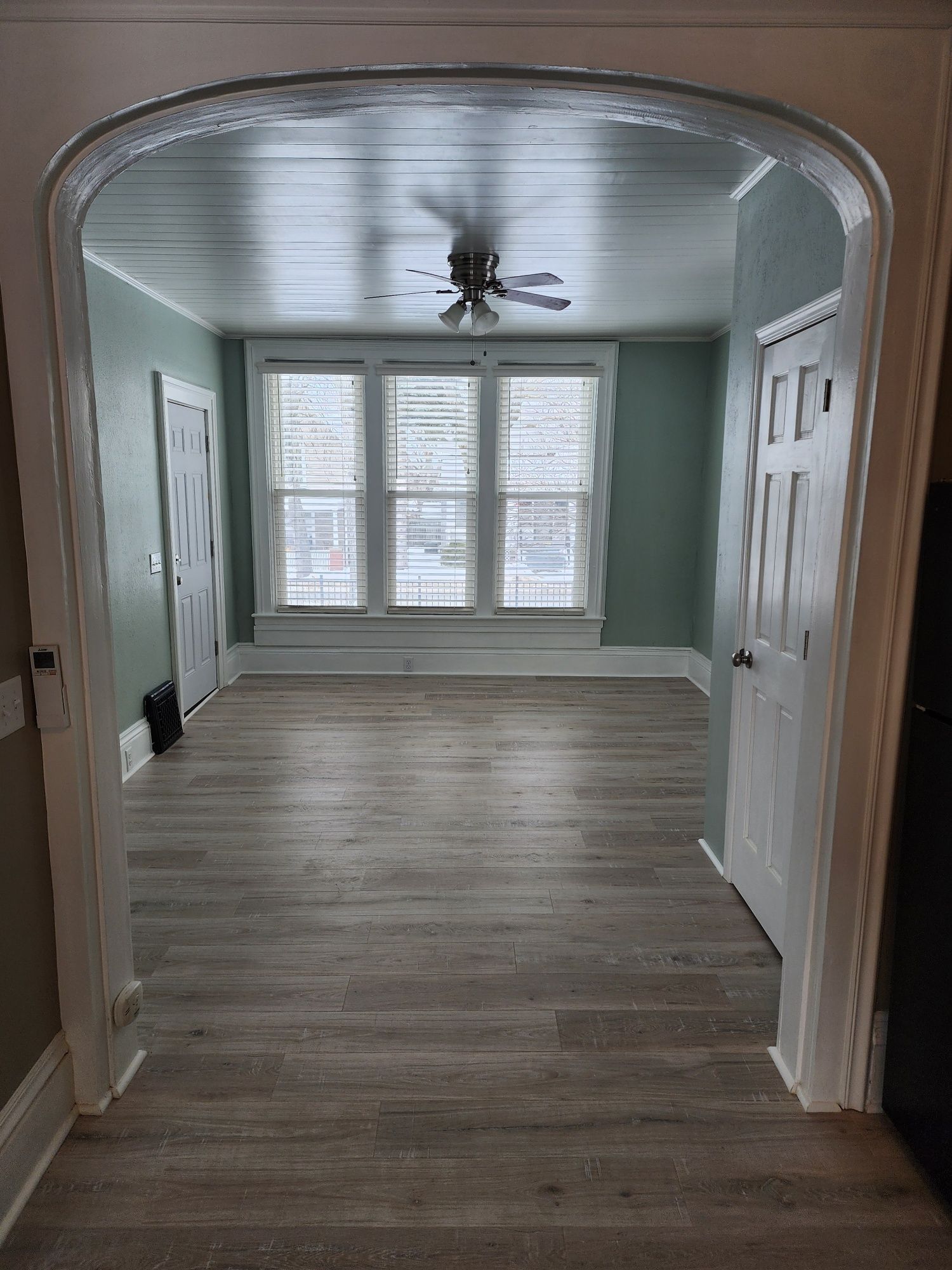 Interior view of a room with light-colored flooring, windows, and two doors. Archway entrance.