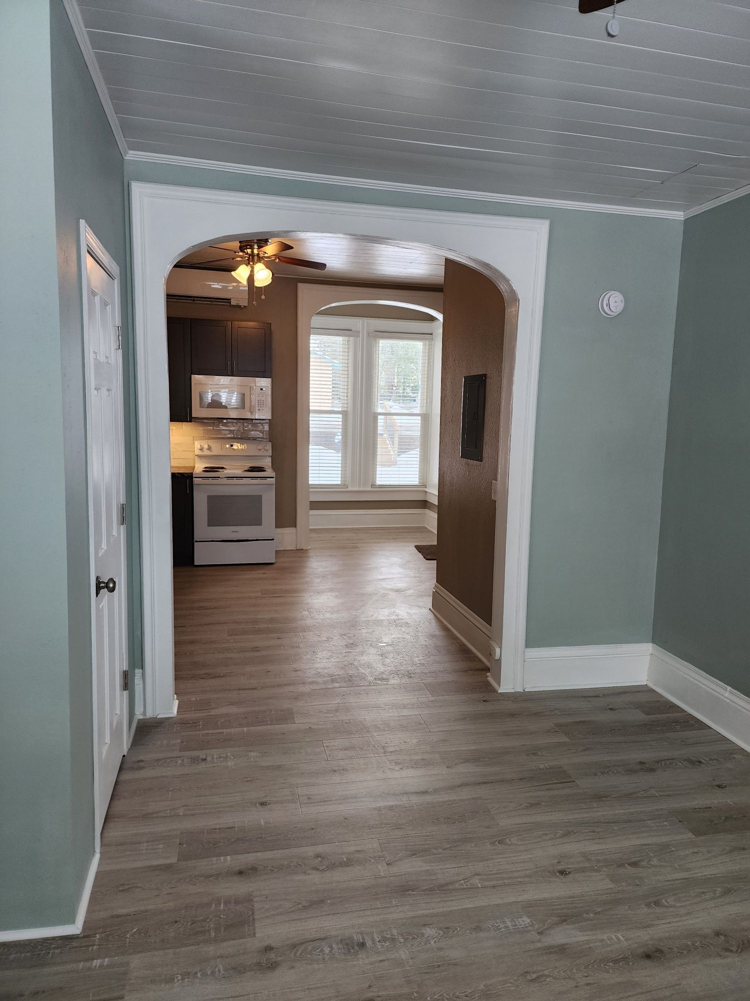 Interior view of a home with open archway leading to kitchen. Light wood-look flooring and light blue walls.