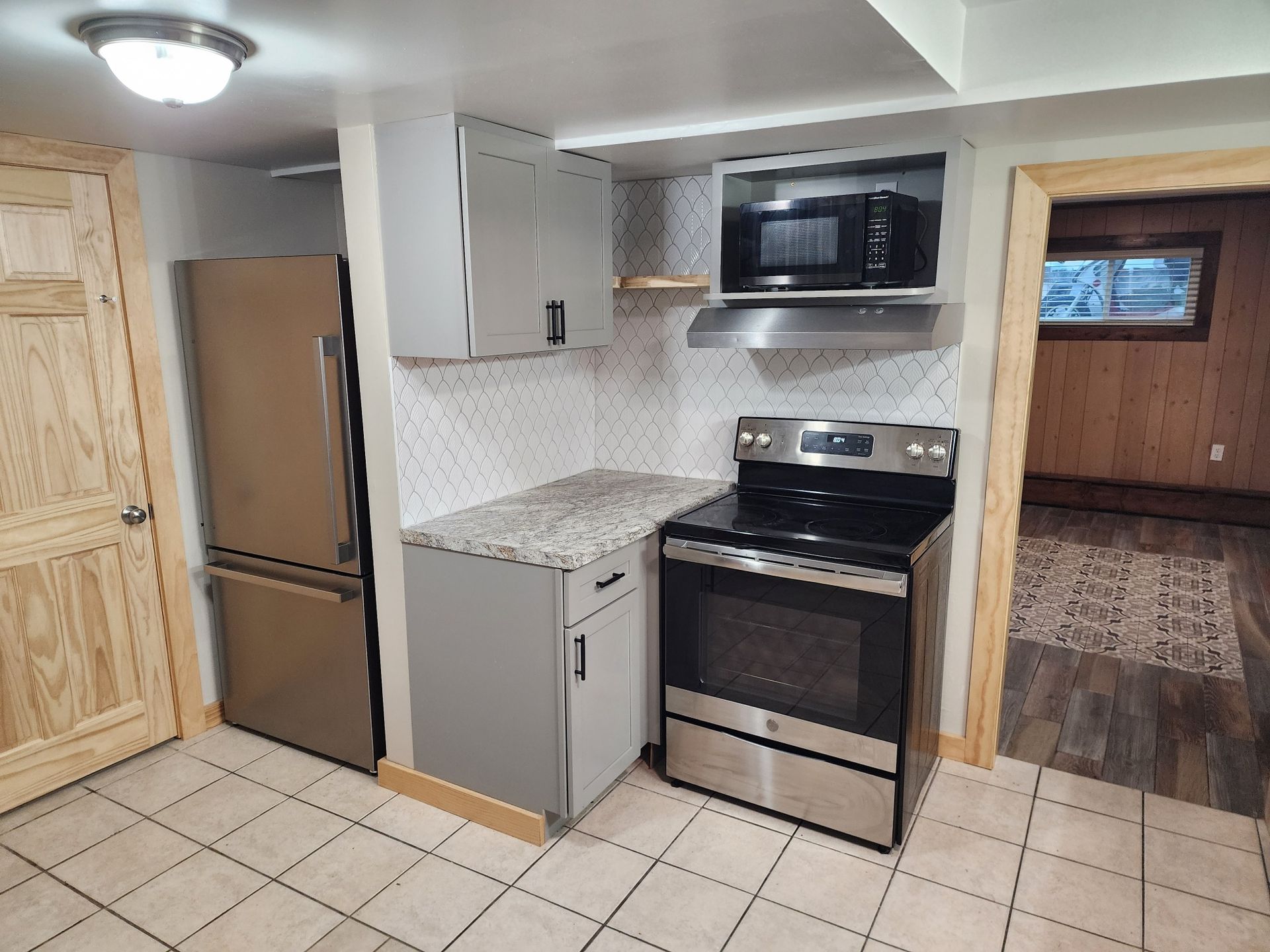 Small kitchen with stainless steel appliances, grey cabinets, and tiled backsplash.
