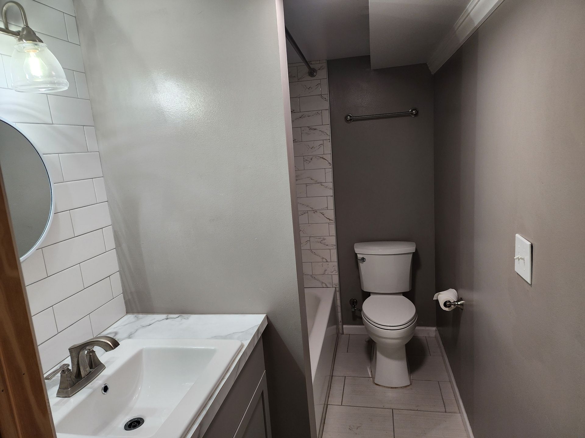 Bathroom with a toilet, sink, and shower/tub. Gray and white color scheme.