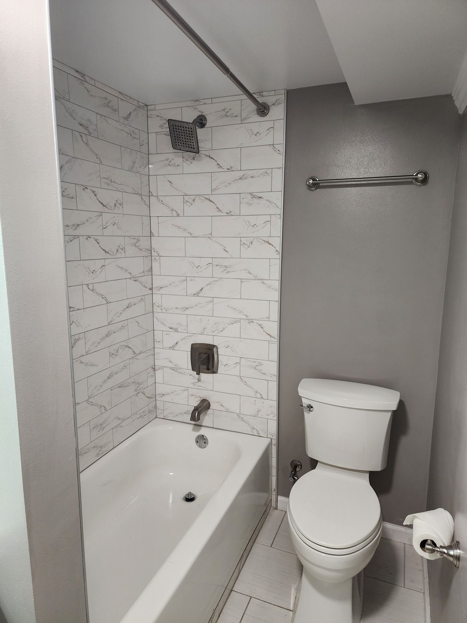 Bathroom with white bathtub, toilet, and patterned shower tile. Gray walls and silver fixtures.