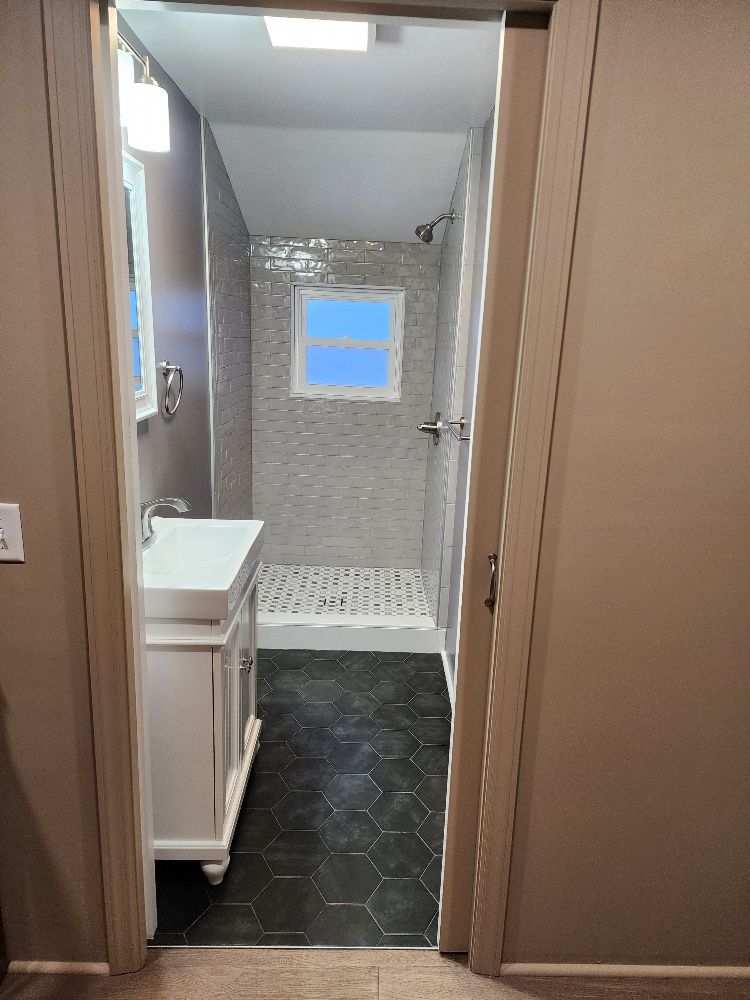 Bathroom with white vanity, gray tile shower, and dark hexagonal floor tiles.