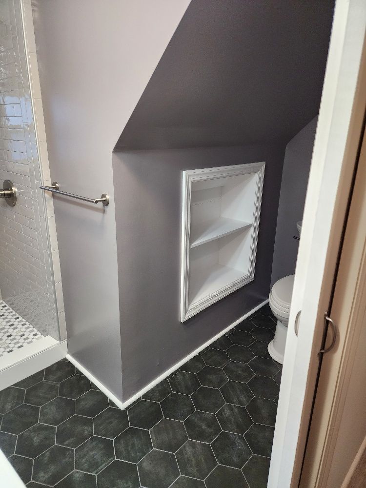 Bathroom with dark gray walls, white trim, recessed shelf, toilet, black hexagon tile floor, and shower.