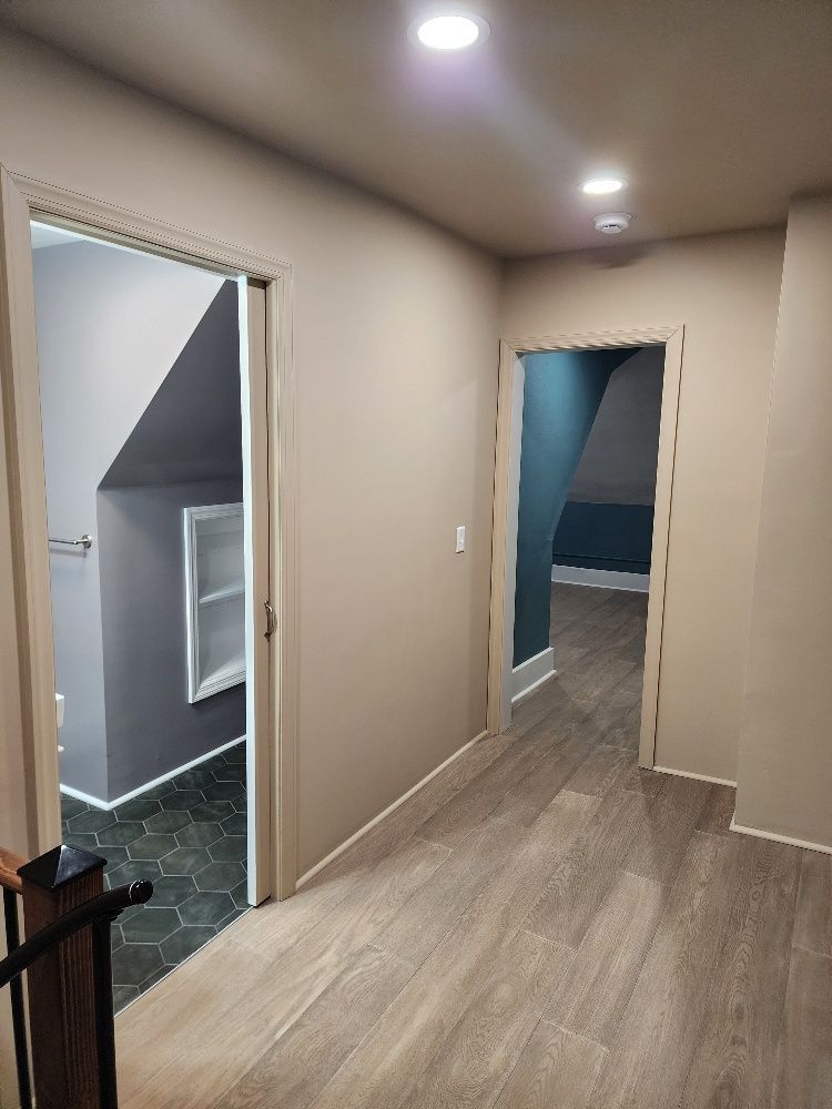 Hallway with two doorways, one leading to a gray-walled room, and another to a blue-walled room. Wooden floors and recessed lighting.