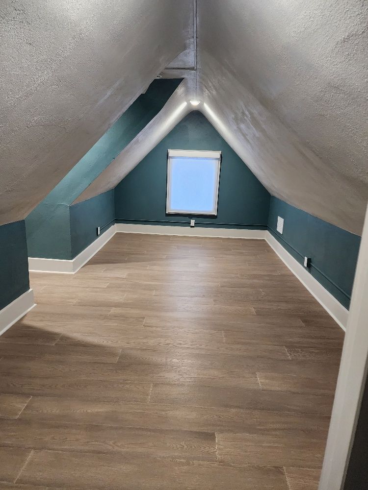 Attic room with sloped walls painted teal, small window, wood-look floor, and white trim.