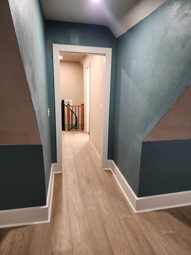 Narrow hallway with teal walls, light wood floor, and doorway leading to another hallway.