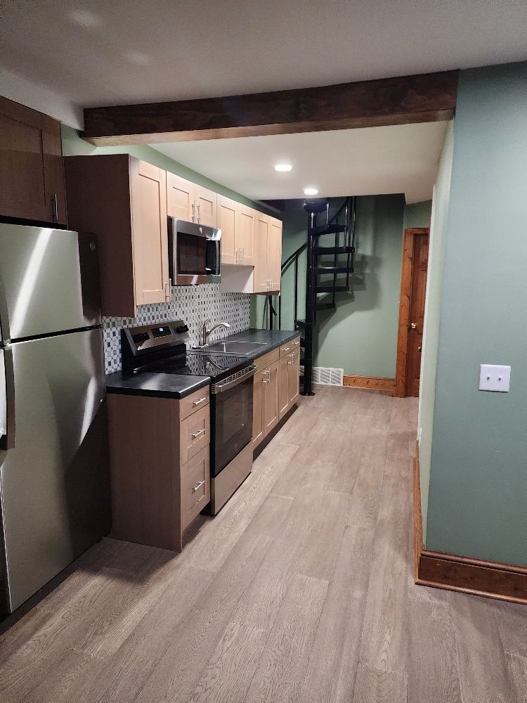 Kitchen with stainless steel appliances, light wood cabinets, and a spiral staircase to an upper level.