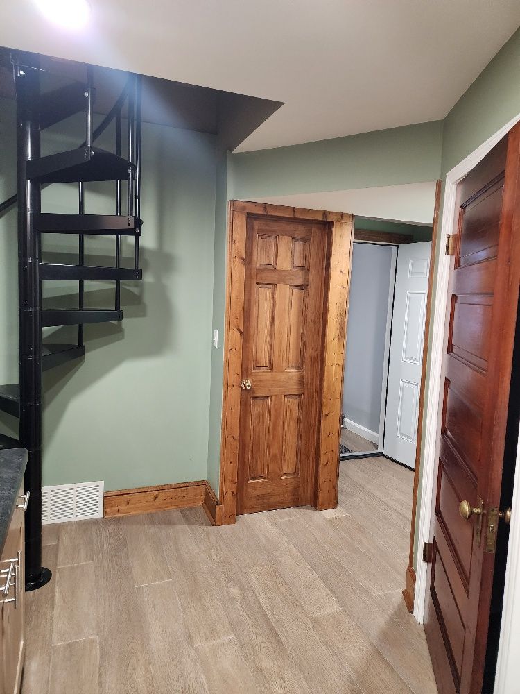 Interior with a spiral staircase, wooden doors, and light-colored flooring; sage-green walls.