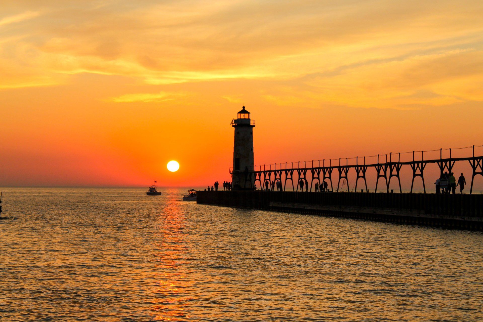 Sunset over a lake with a lighthouse and pier. The sky is fiery orange.