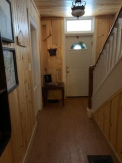 Narrow hallway with wood paneling, front door, staircase, and small table.