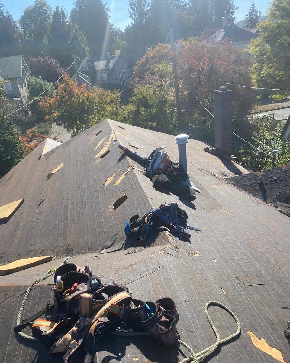 Roofer on a sloped roof removes old shingles. Tools and safety harness are visible.