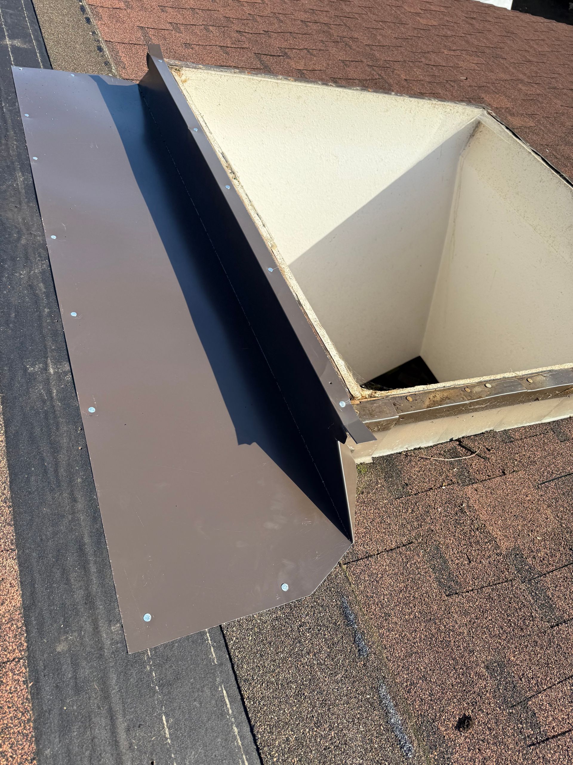 Brown metal flashing around a white skylight opening on a shingled roof.