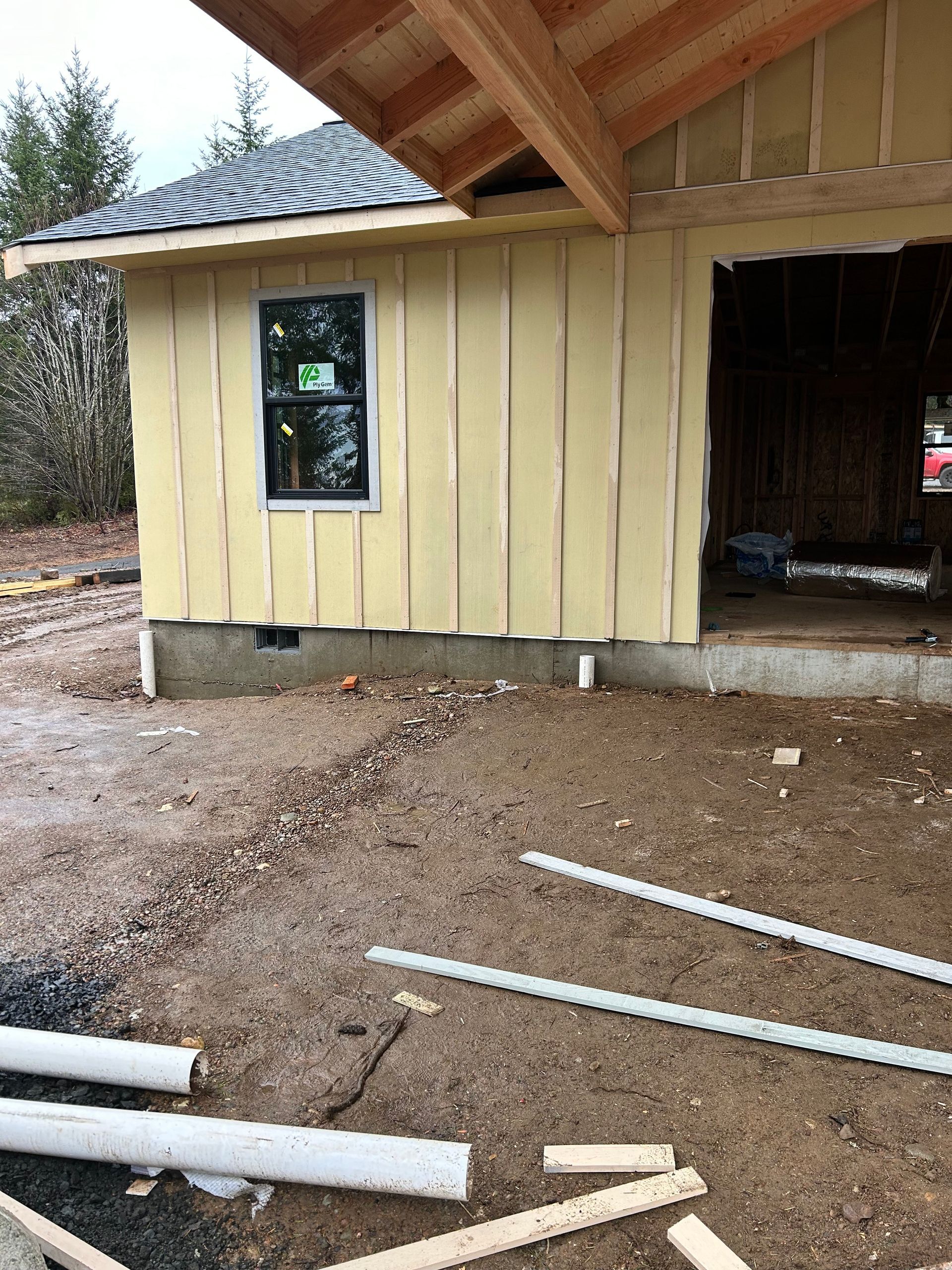 Building under construction with yellow siding, a window, and open doorway, on a gravel surface.