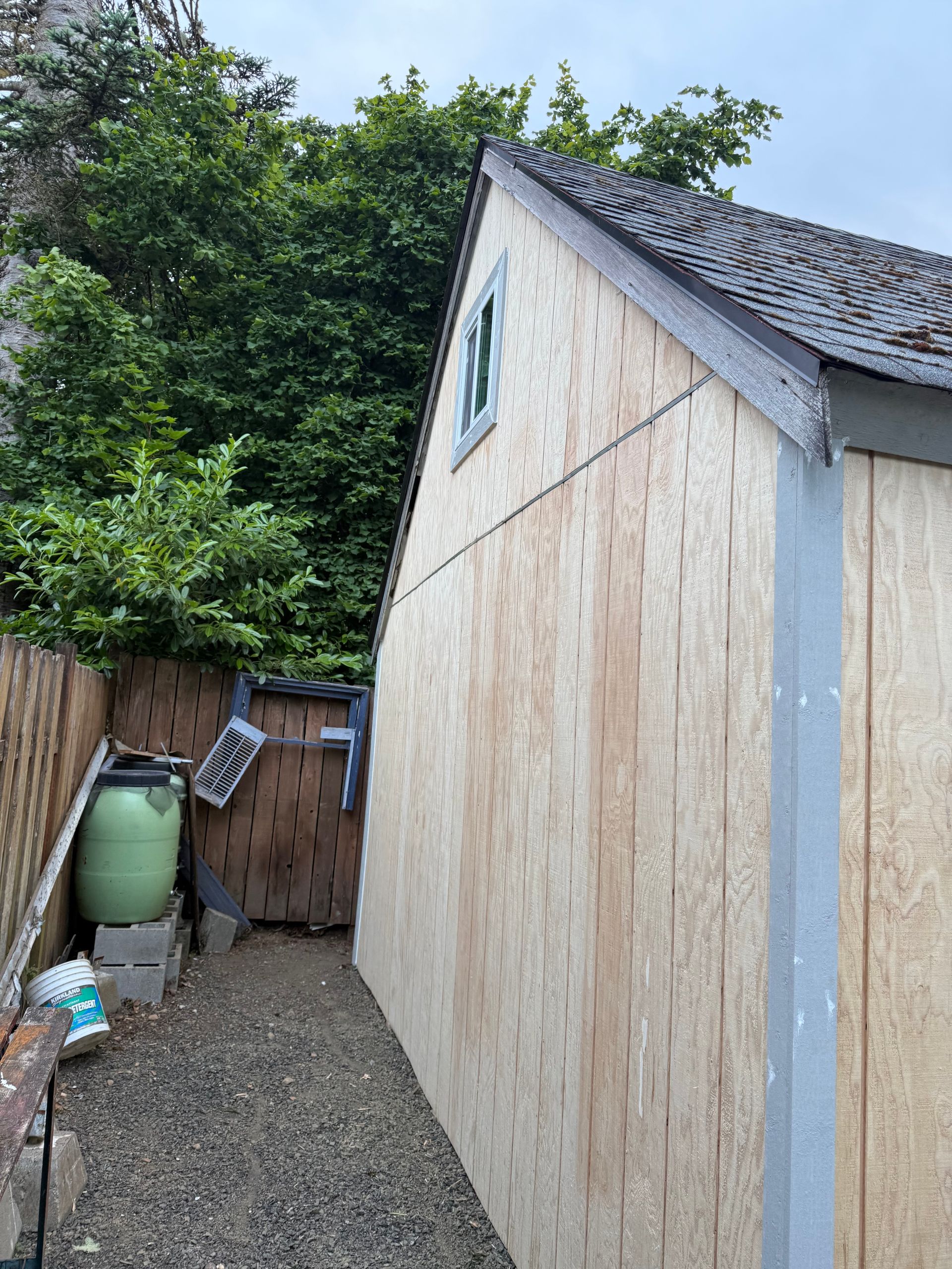 Side view of a small shed with an angled roof and small window next to a gravel path and wooden fence.
