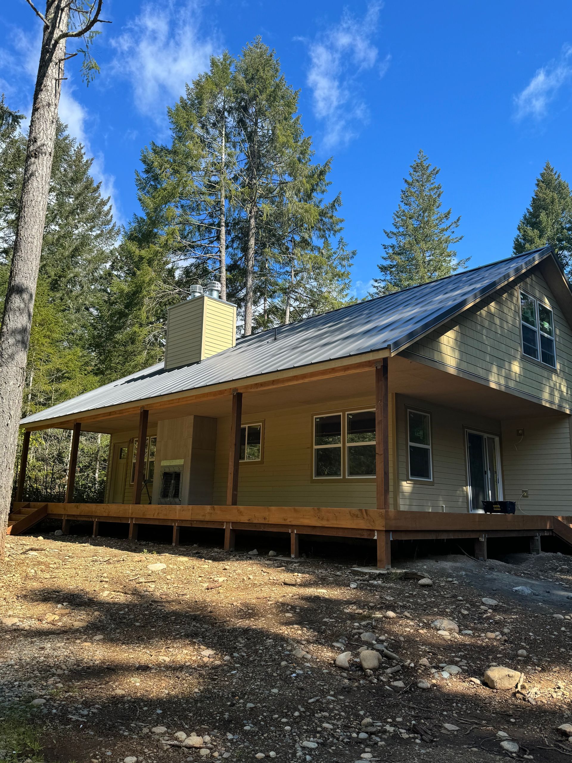 Cabin with a wraparound porch, surrounded by trees under a blue sky.