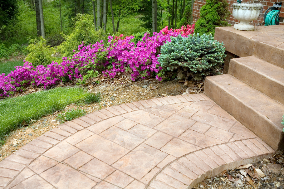 Brick-pattern stamped concrete walkway bordered by vibrant landscaping, creating a timeless and inviting design.