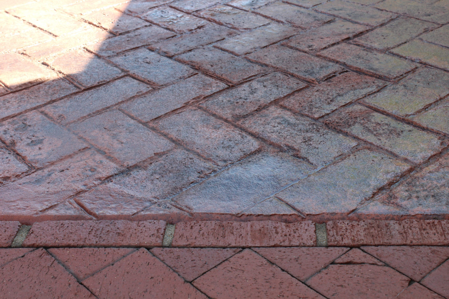 Red herringbone stamped concrete with a brick border, combining classic patterns with durable outdoor design.