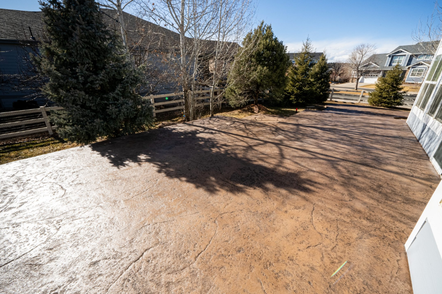 A large stamped concrete patio in a residential backyard with a textured surface and natural brown c
