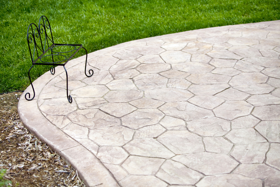 Stamped concrete patio with a decorative stone pattern and wrought iron chair in a backyard setting.
