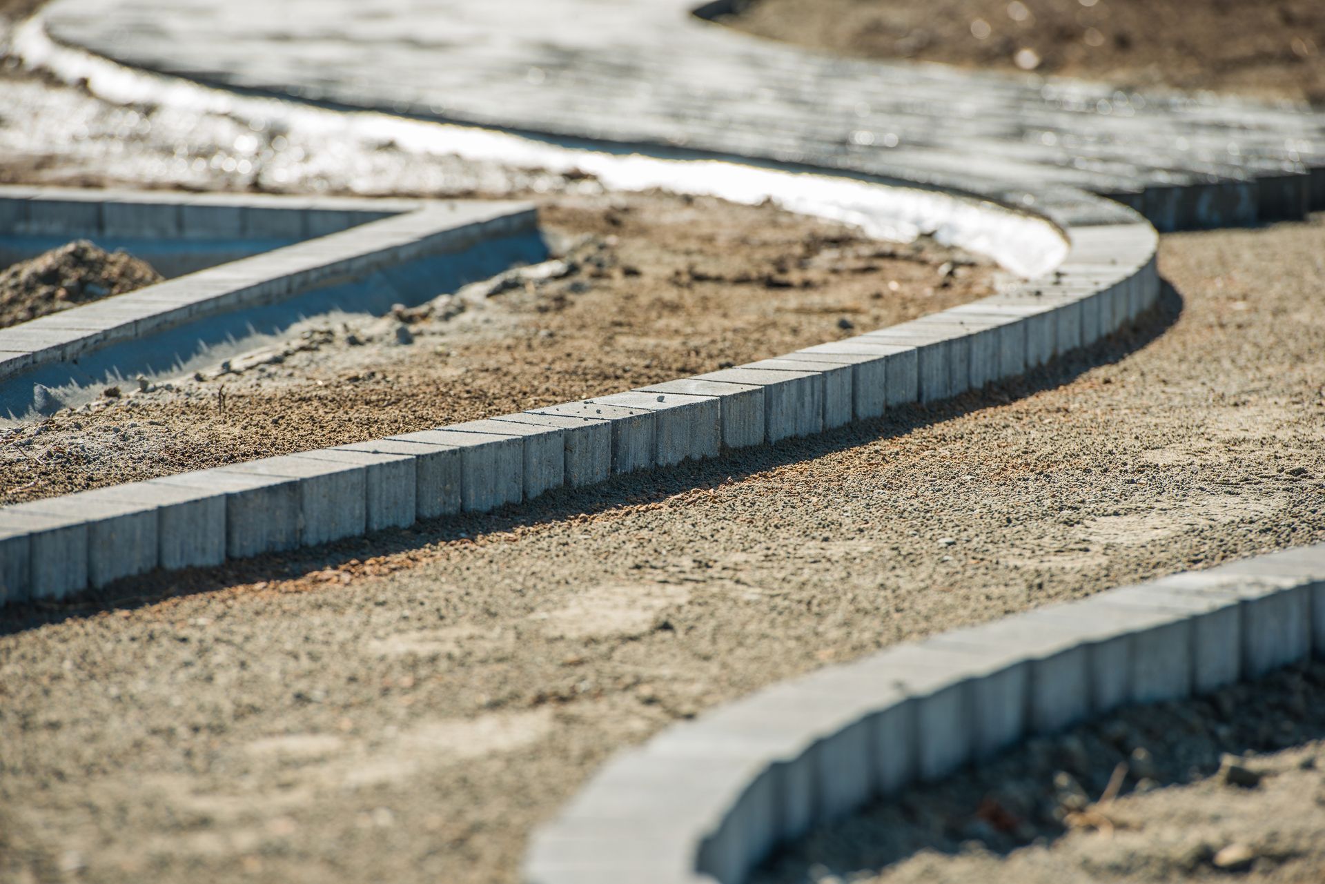 A concrete curb is being installed on a dirt road.