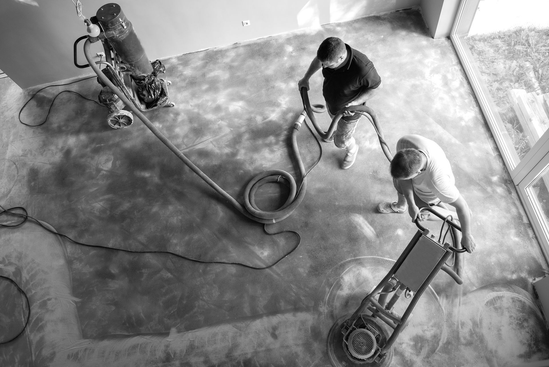 A black and white photo of three men using vacuum cleaners on a concrete floor.