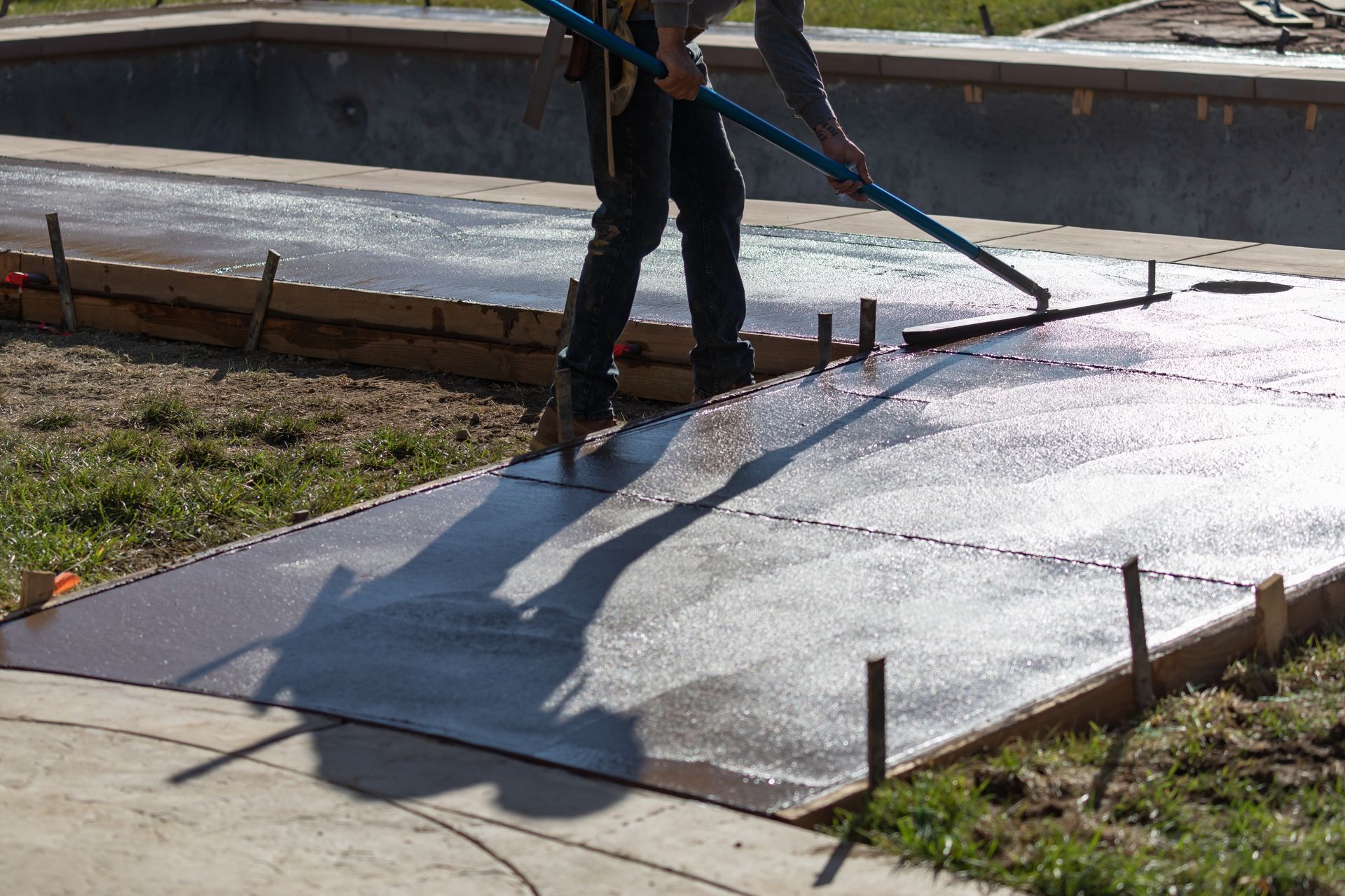 A man is spreading concrete on a sidewalk near a pool