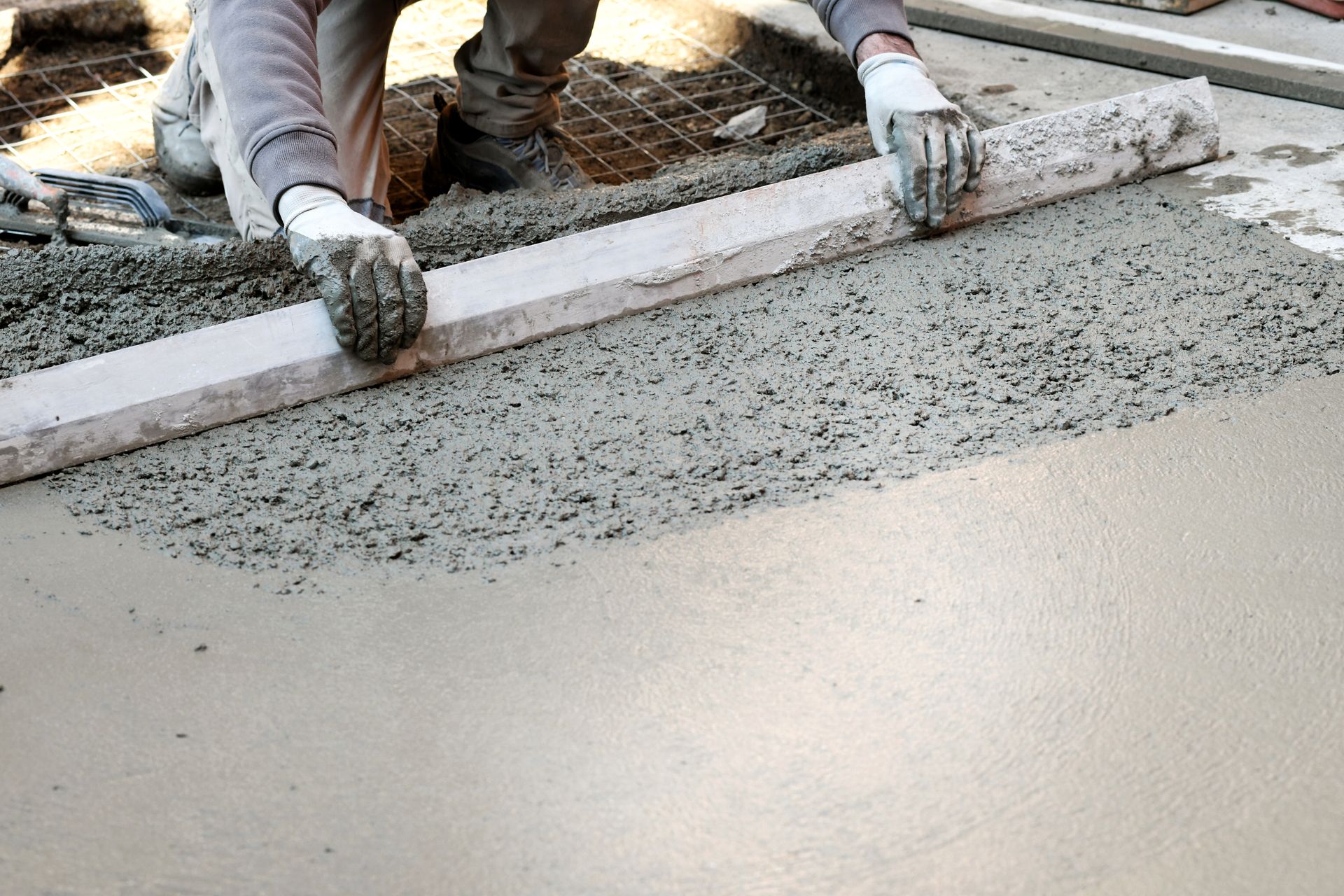 A man is laying concrete on the ground with a level.