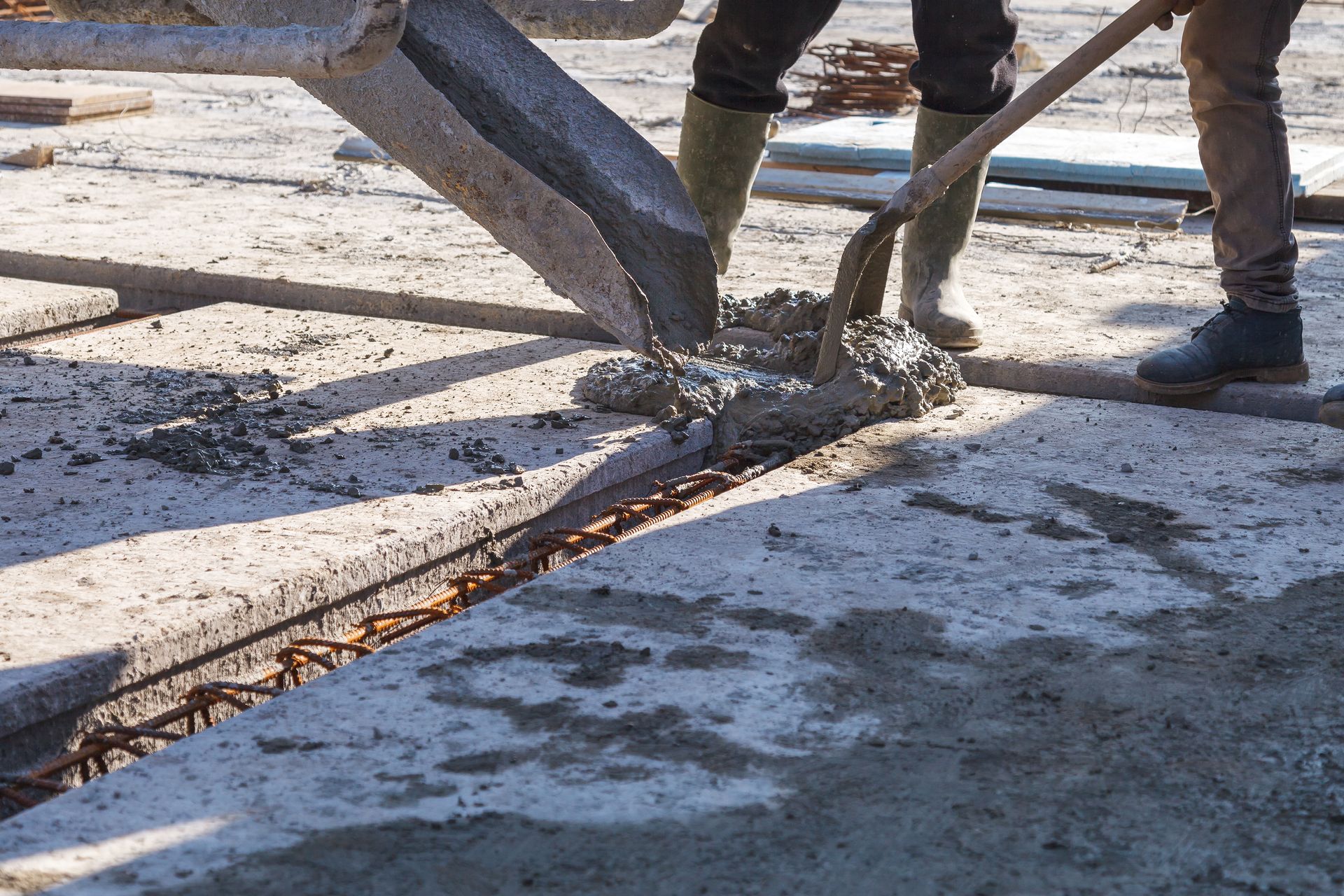 A man is pouring concrete into a hole in the ground with a shovel.